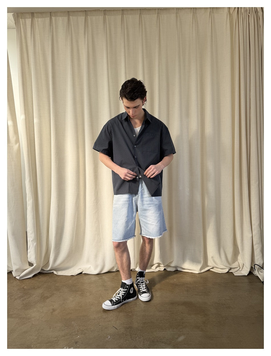 Model wearing a black short-sleeve pinstriped button-up shirt with a chest pocket and light denim shorts.