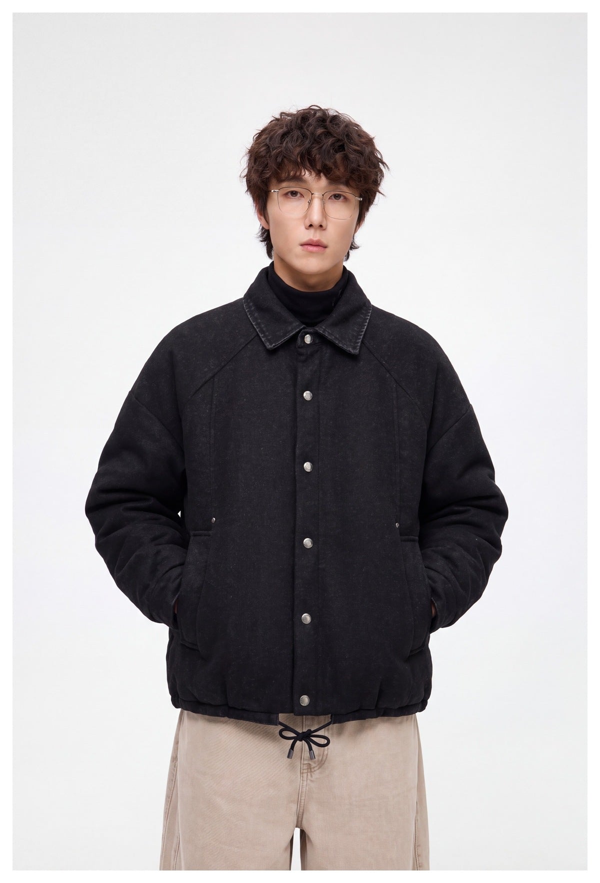 Model wearing a black button-front jacket with a pointed collar and drawstring hem, shown from the front.