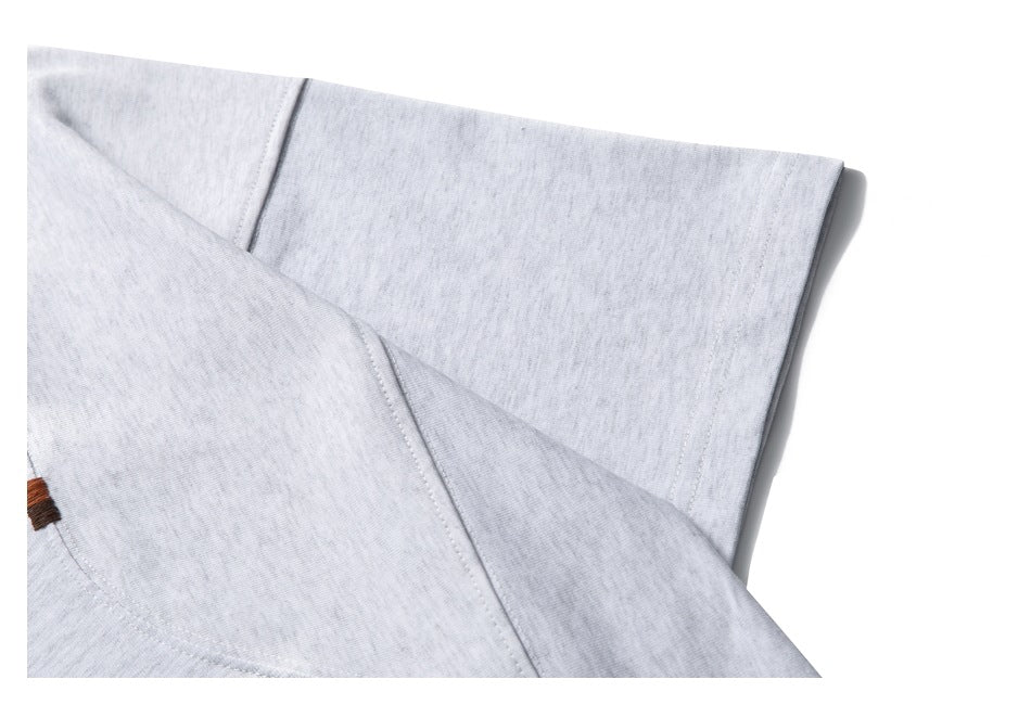 Close-up of light gray knit fabric with a folded seam and a small brown stitch detail.