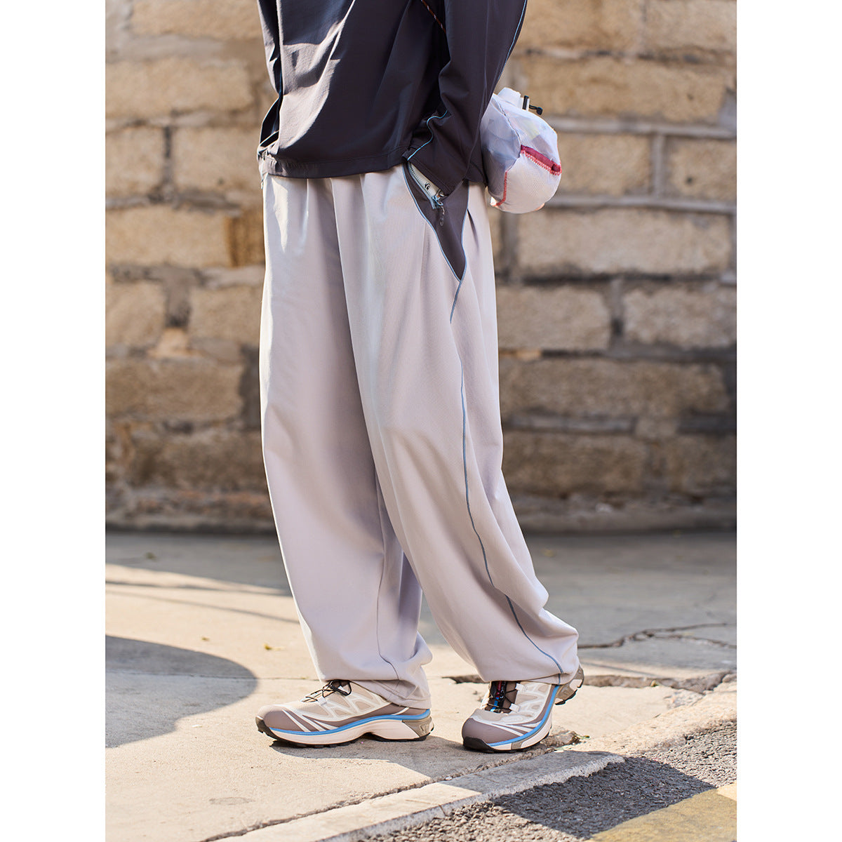 Close view of loose light-gray pants with blue contrast piping and a zippered side pocket.