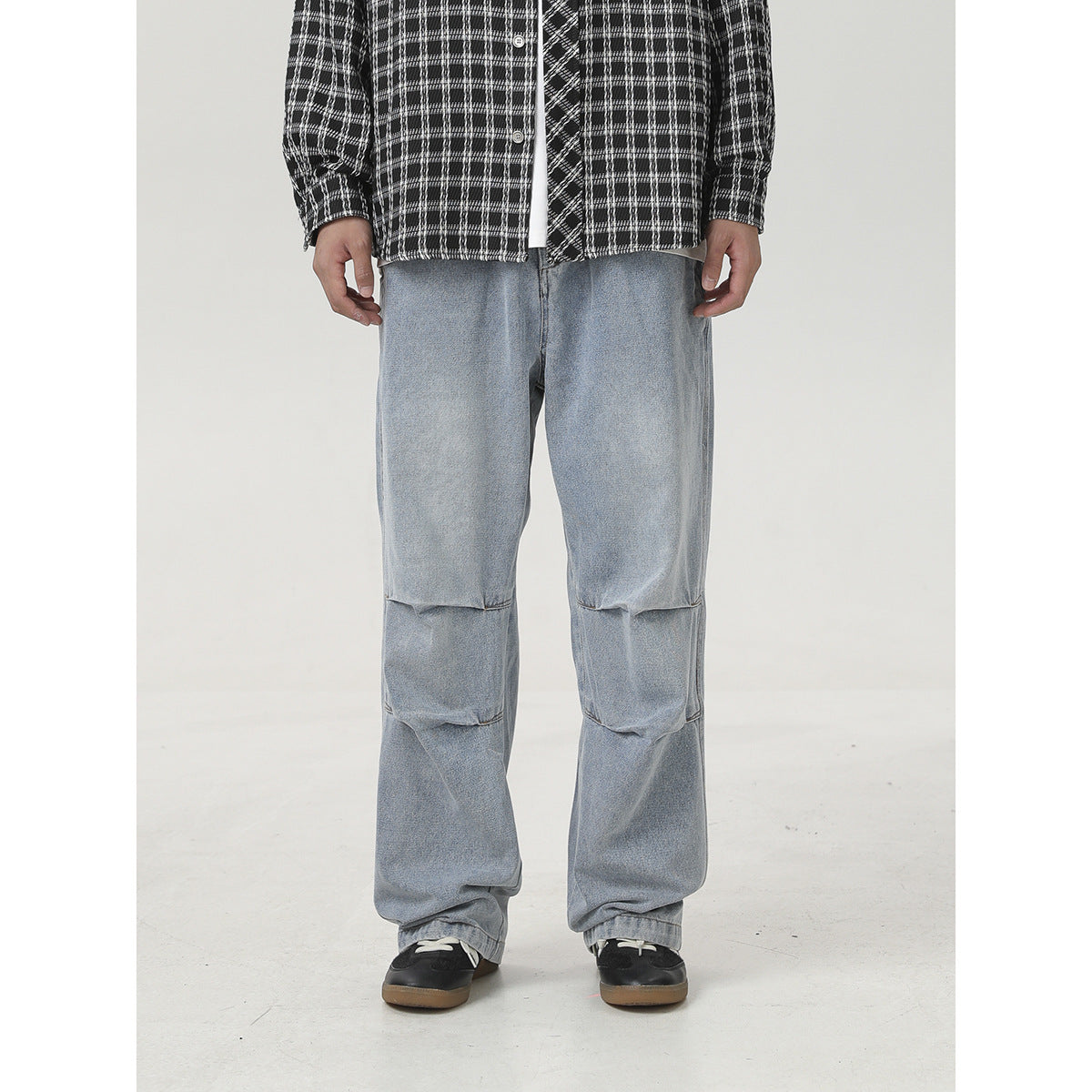 Front view of loose light-wash jeans with layered knee seams, worn with a black-and-white plaid shirt.