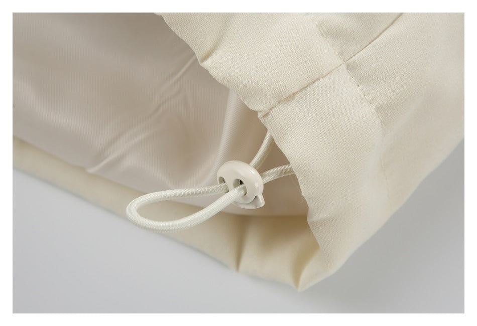 Close-up of the cream jacket's hem drawcord loop and round cord stopper.