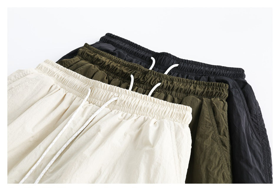 Three pairs of drawstring pants arranged together in cream, olive green, and black.