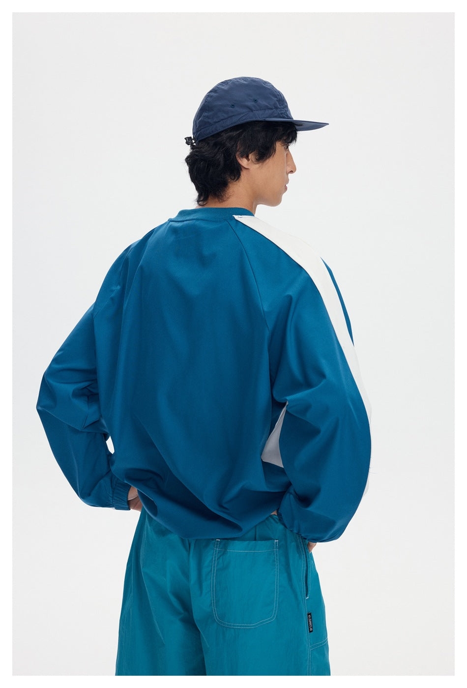 Rear view of a model wearing a teal pullover with white shoulder and sleeve panels and teal shorts.