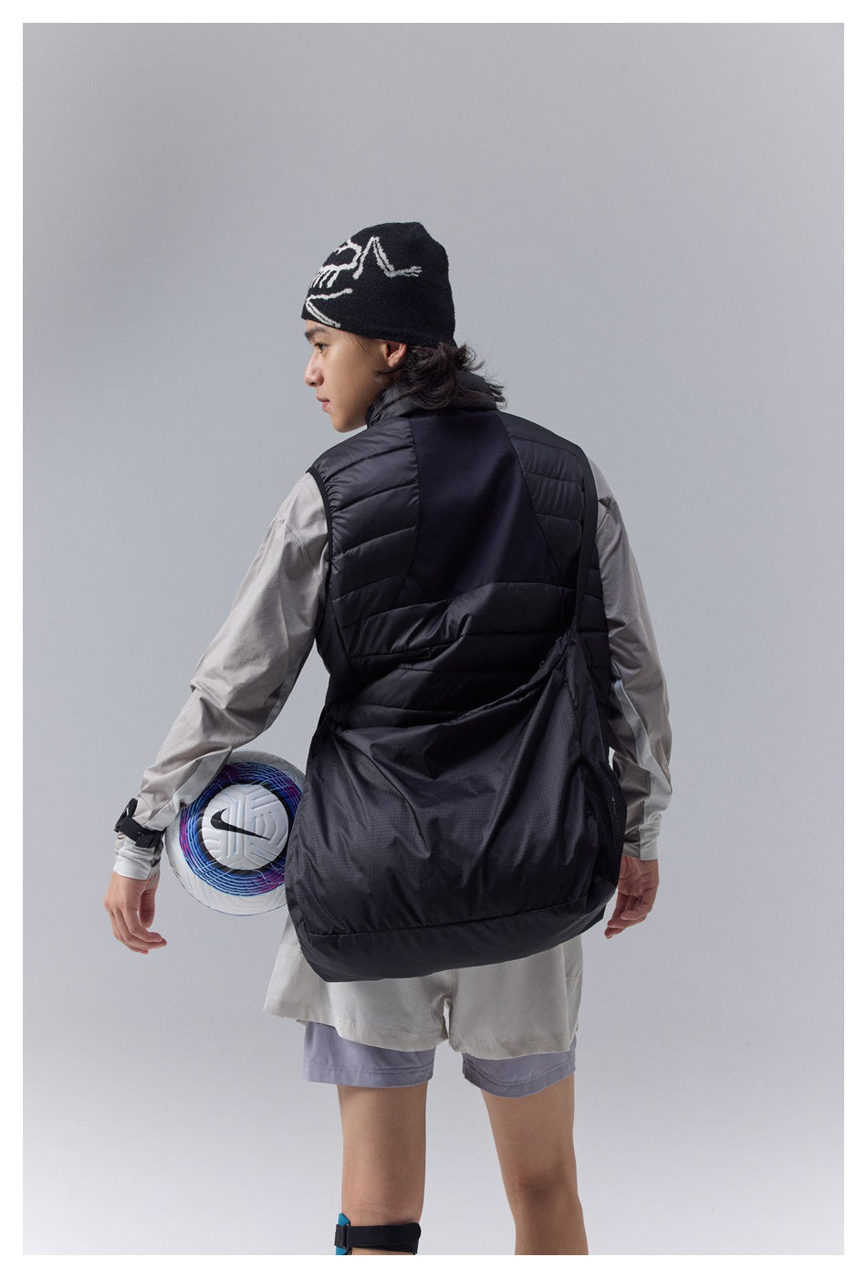 Rear view of a model wearing a black quilted vest with a large black lower-back panel over a light gray top.