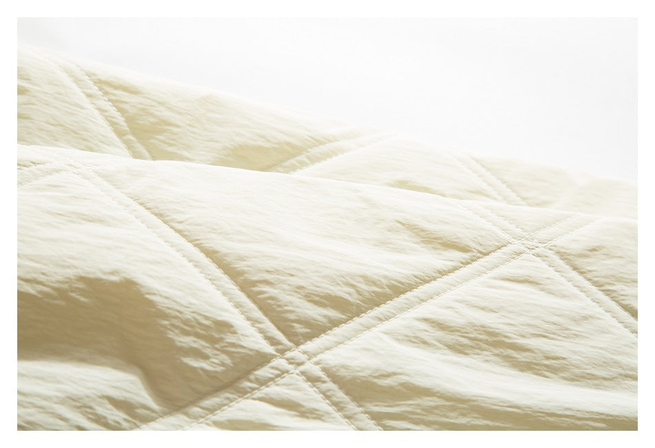 Close-up of the ivory jacket's softly textured fabric and intersecting quilted stitching.