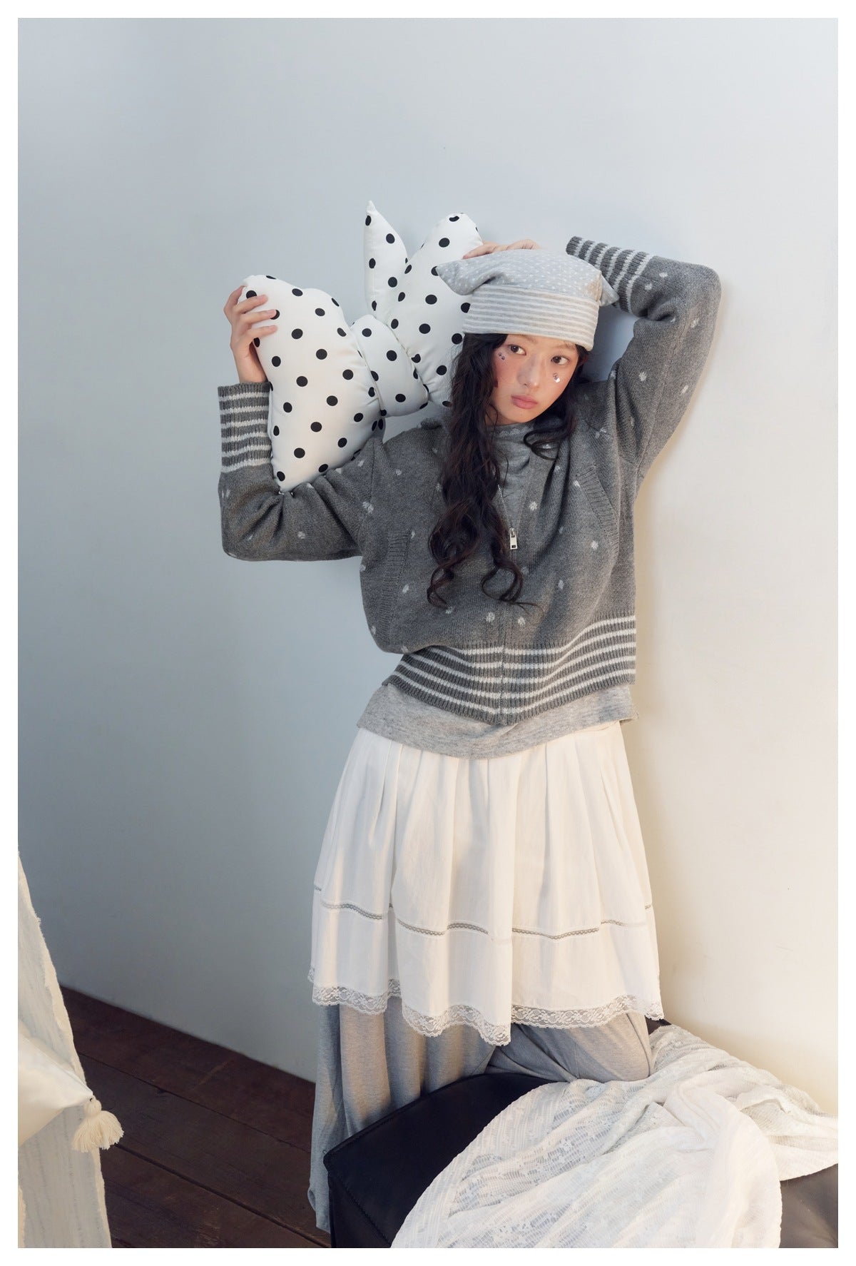 Model poses in a gray zip cardigan with small white motifs and striped trim, paired with a tiered white dress.