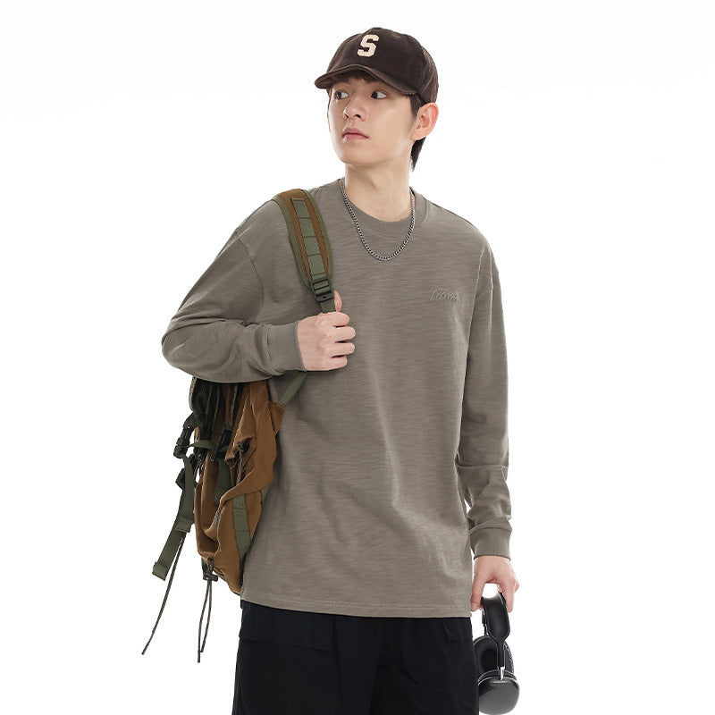 Model wearing a taupe long-sleeve crewneck shirt with a dark cap and backpack against a white background.