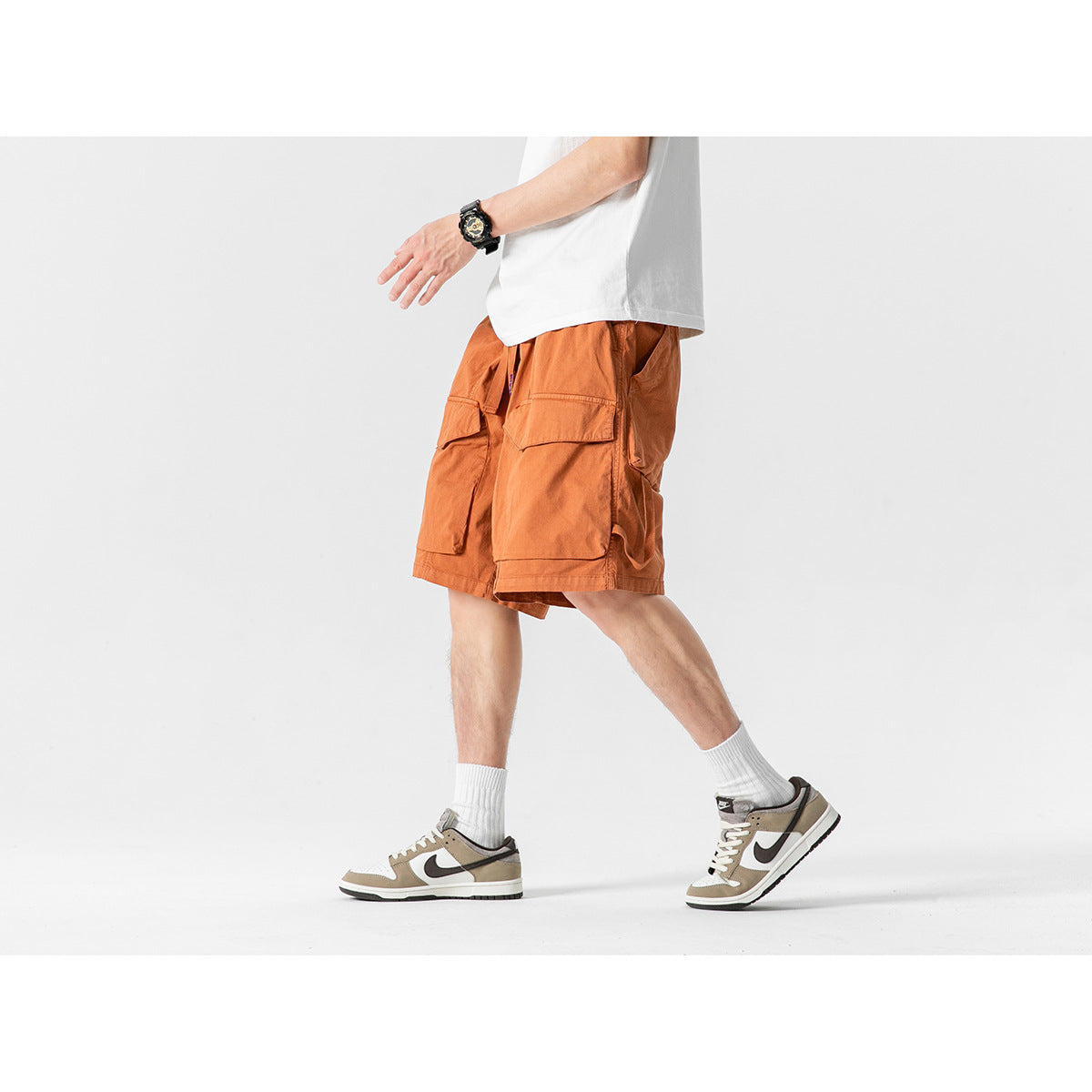 Side view of a model walking in rust-orange cargo shorts with large flap pockets and a white T-shirt.