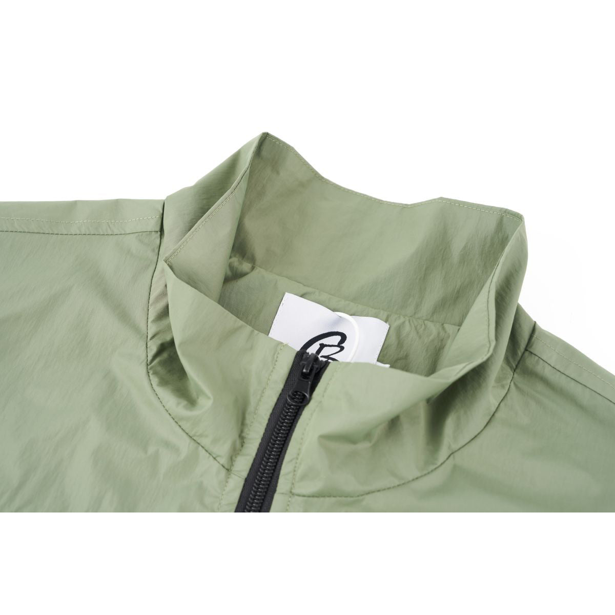 Close-up of a pale sage-green jacket's stand collar and black front zipper, with a small neck label visible.