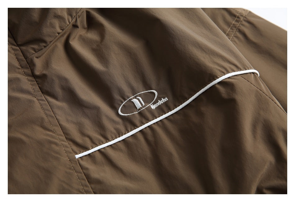 Close-up of a brown jacket showing white piping and a small embroidered oval logo.