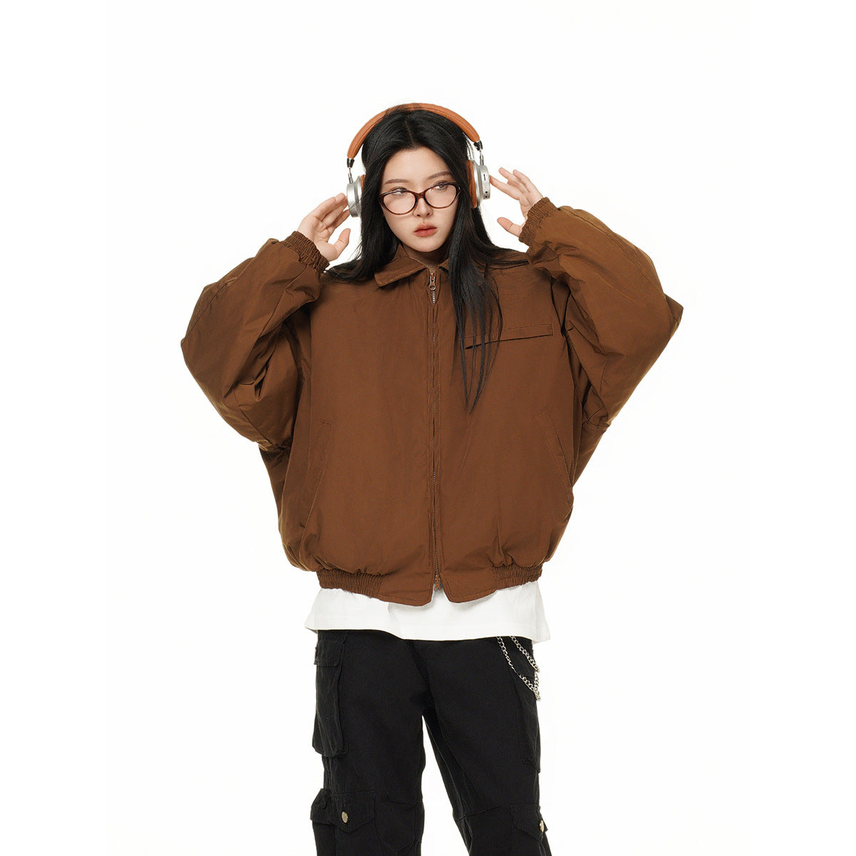 Front view of a model wearing an oversized brown zip jacket with a collar, chest pocket and gathered cuffs and hem.
