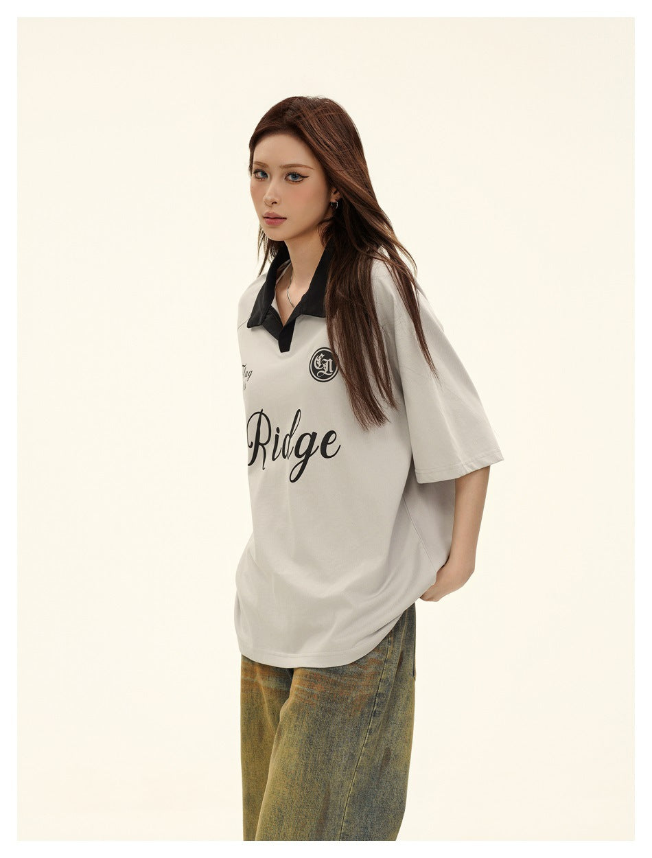 Model wearing an oversized light gray polo with a black collar and black chest graphics, paired with loose jeans.