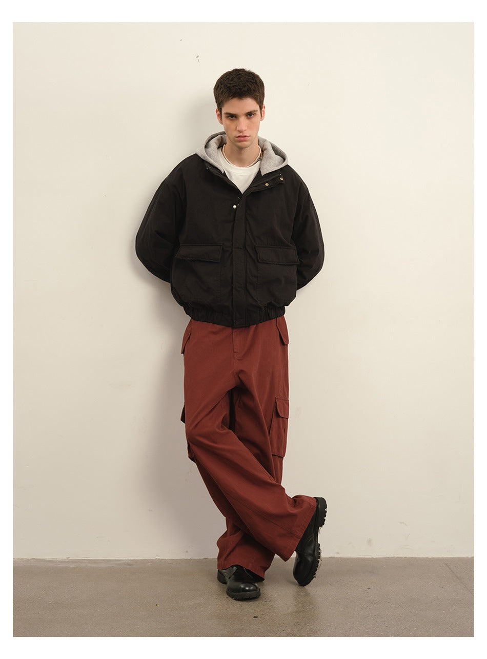 Model wearing a black hooded jacket with flap pockets, rust cargo pants, and black boots.