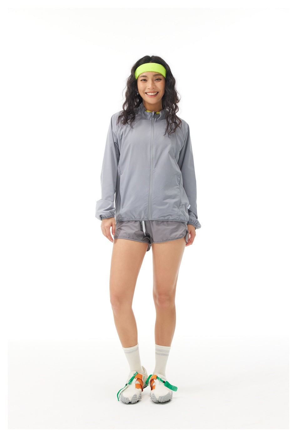 Front view of a model wearing a zipped light gray jacket and matching shorts with a neon yellow headband.