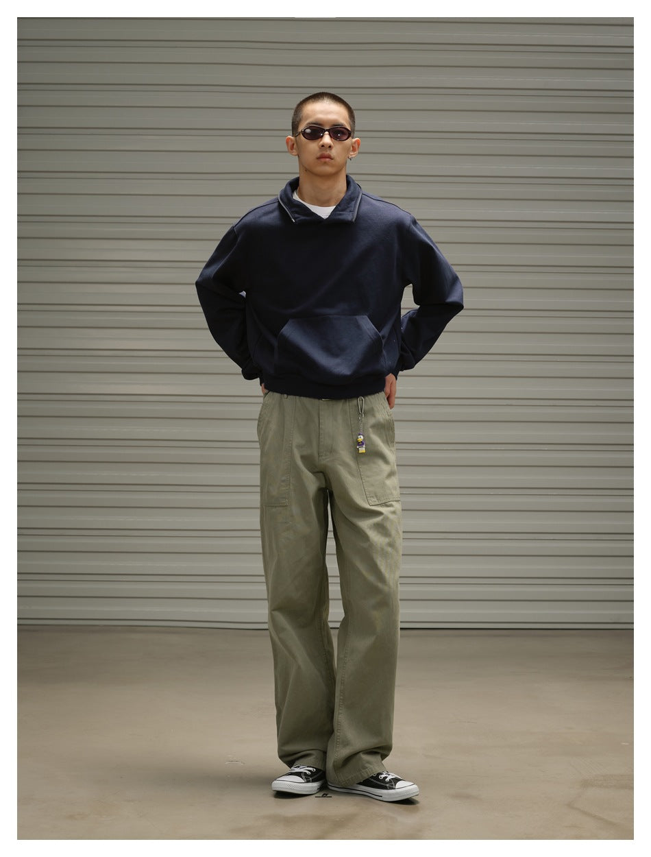 Model wearing a navy collared pullover with a large front pouch pocket and loose olive trousers.
