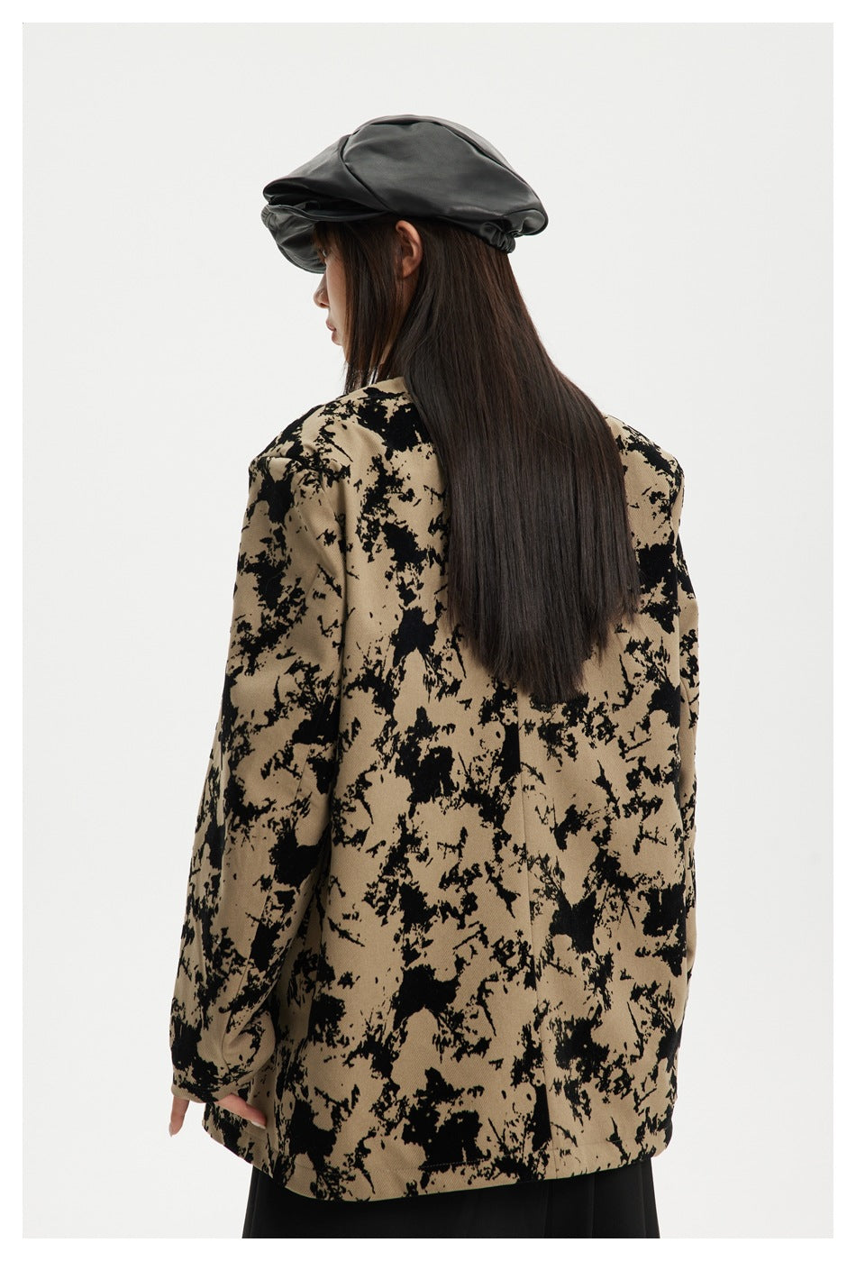 Back view of a model wearing an oversized tan jacket with an irregular black pattern.