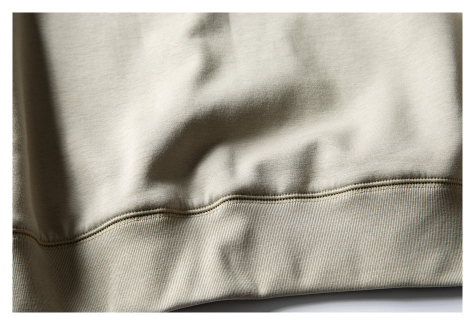 Close-up of a light beige garment's stitched seam and wide ribbed hem band.