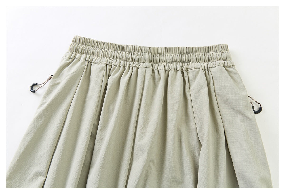 Cropped front view of pale khaki trousers laid flat, with an elastic waistband, pleats, and side drawcord toggles.