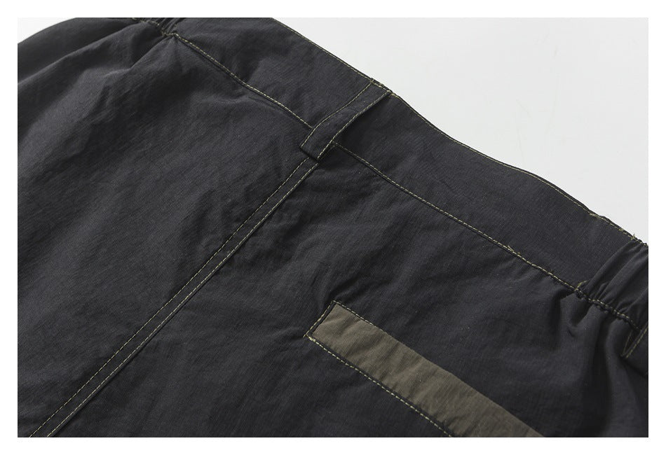Close-up of dark charcoal pants showing the waistband, belt loop, seams, and olive-gray pocket trim.