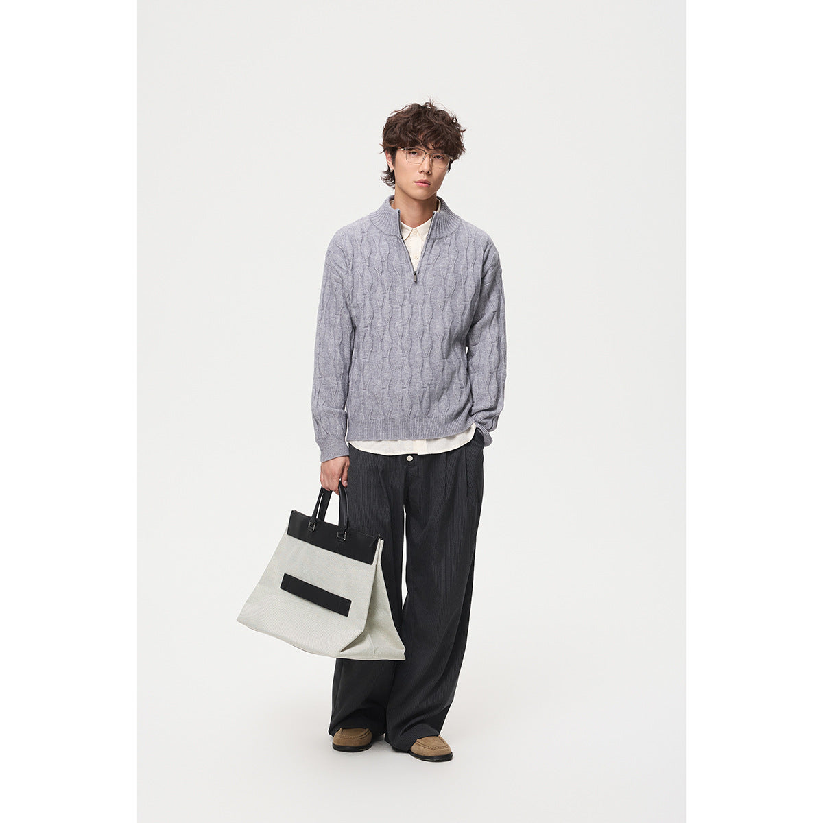 Full-length model wearing a light gray cable-pattern quarter-zip sweater with dark trousers.