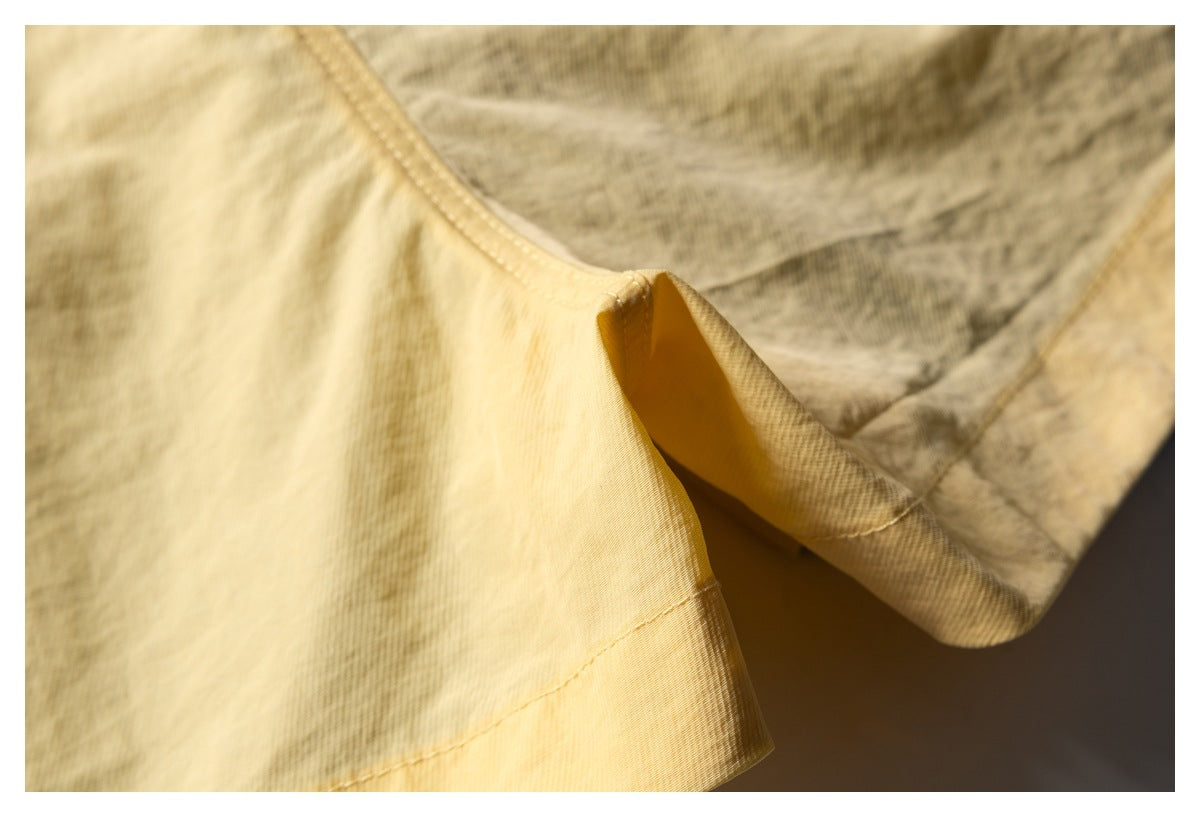 Close-up of a stitched hem and seam on pale yellow patterned shorts.