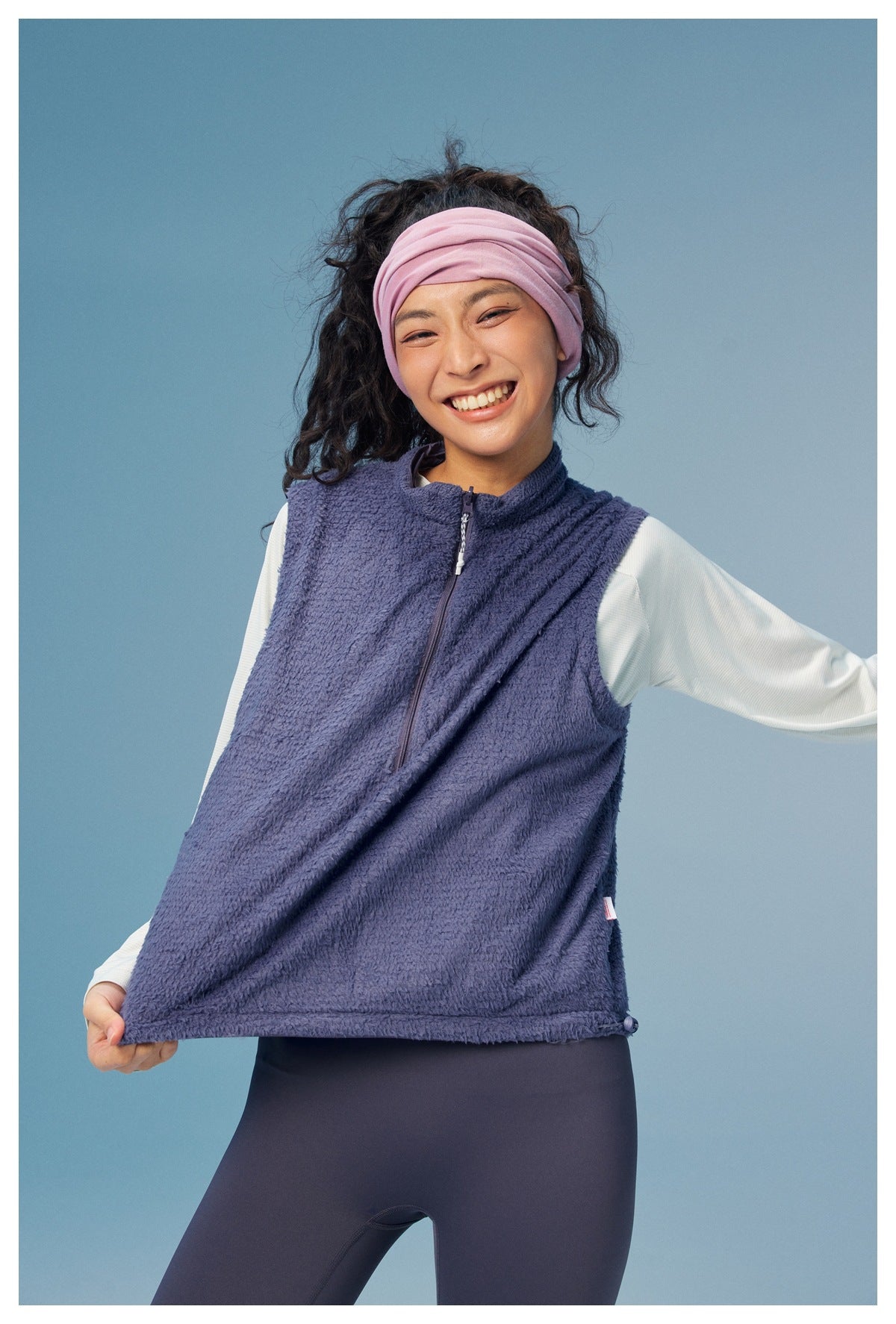 Model wearing a purple sleeveless vest with a high collar and front zipper over a pale long-sleeve top.