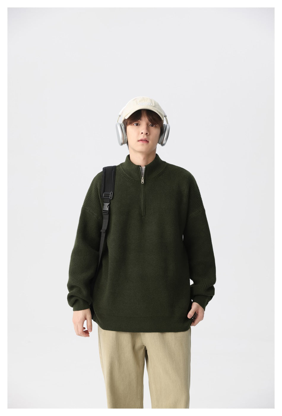Front view of a model wearing a dark olive ribbed quarter-zip sweater and beige trousers with a shoulder bag.