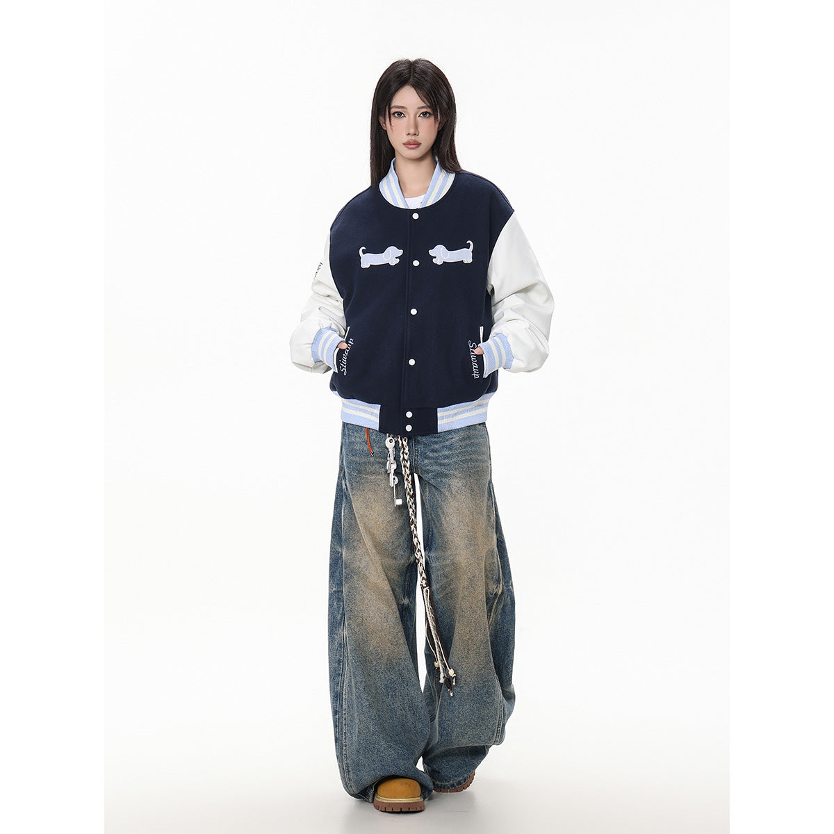 Model wearing a navy varsity jacket with white sleeves, striped blue trim and dog appliqués, styled with baggy jeans.