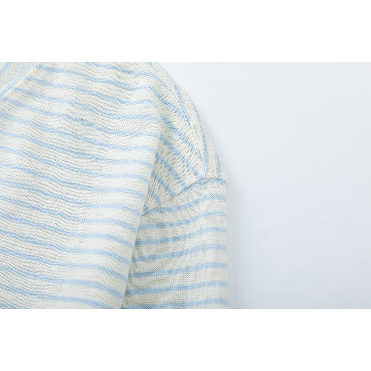 Close-up of the shoulder seam and sleeve on an ivory shirt with thin pale blue stripes.