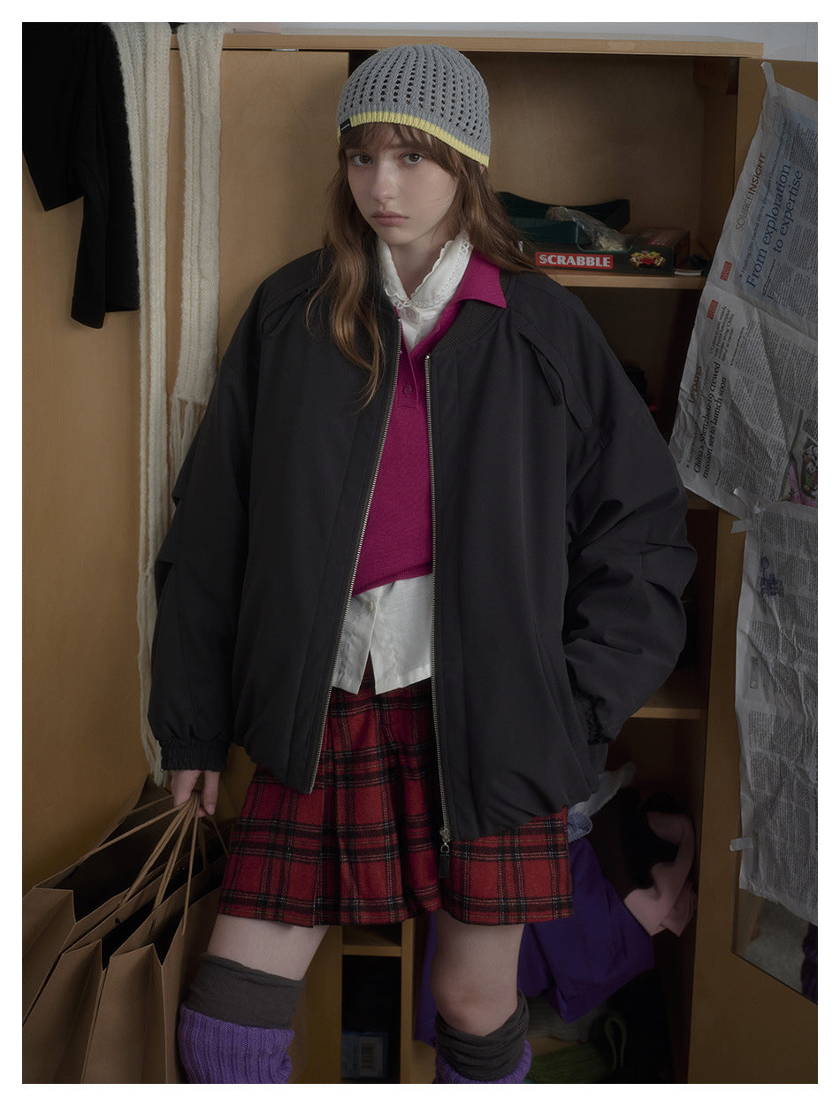 Model wearing an oversized black zip-front jacket over a bright pink top and red plaid shorts, shown from the front.