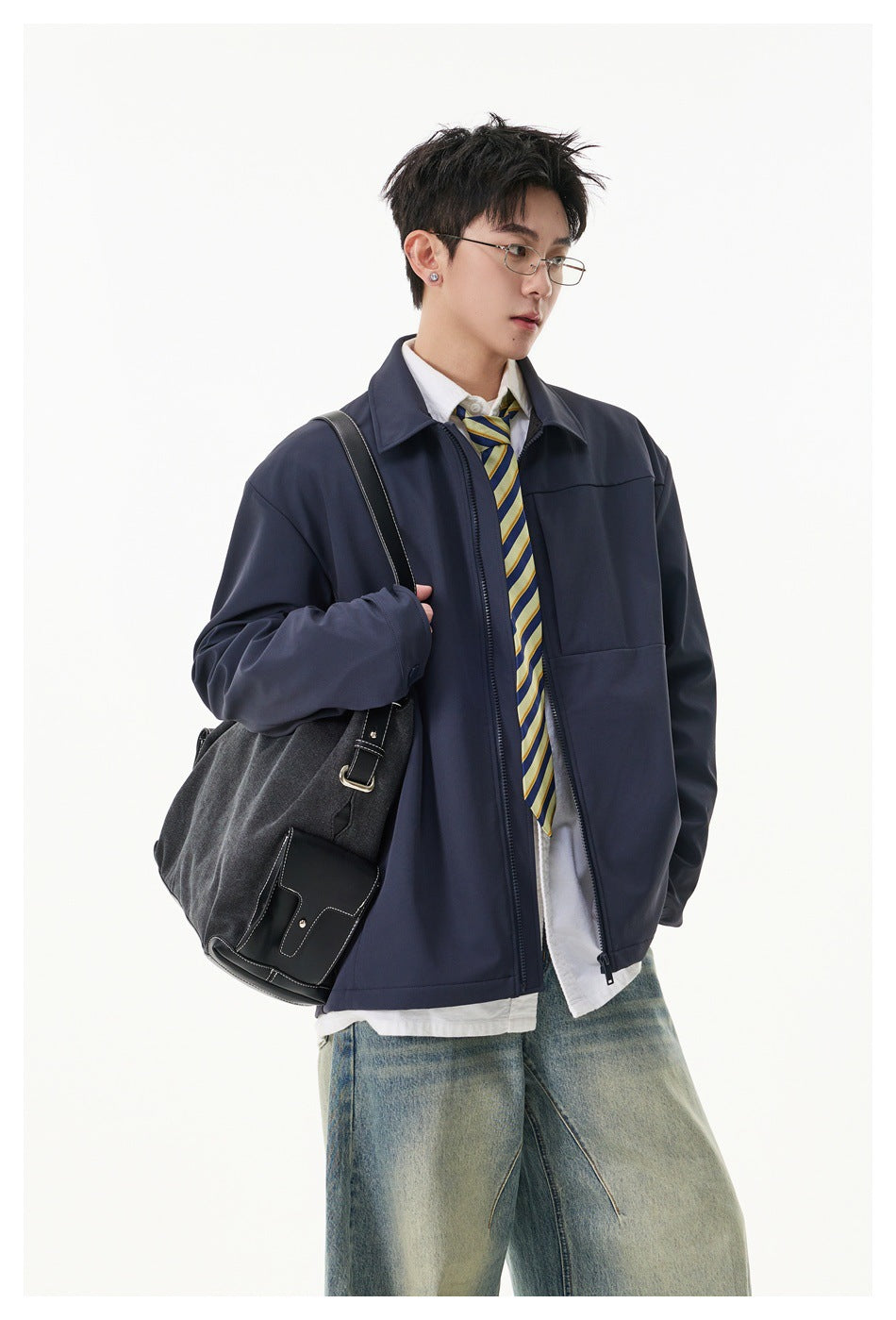 Model wearing a navy zip-front jacket over a white shirt and striped tie, with a dark shoulder bag.