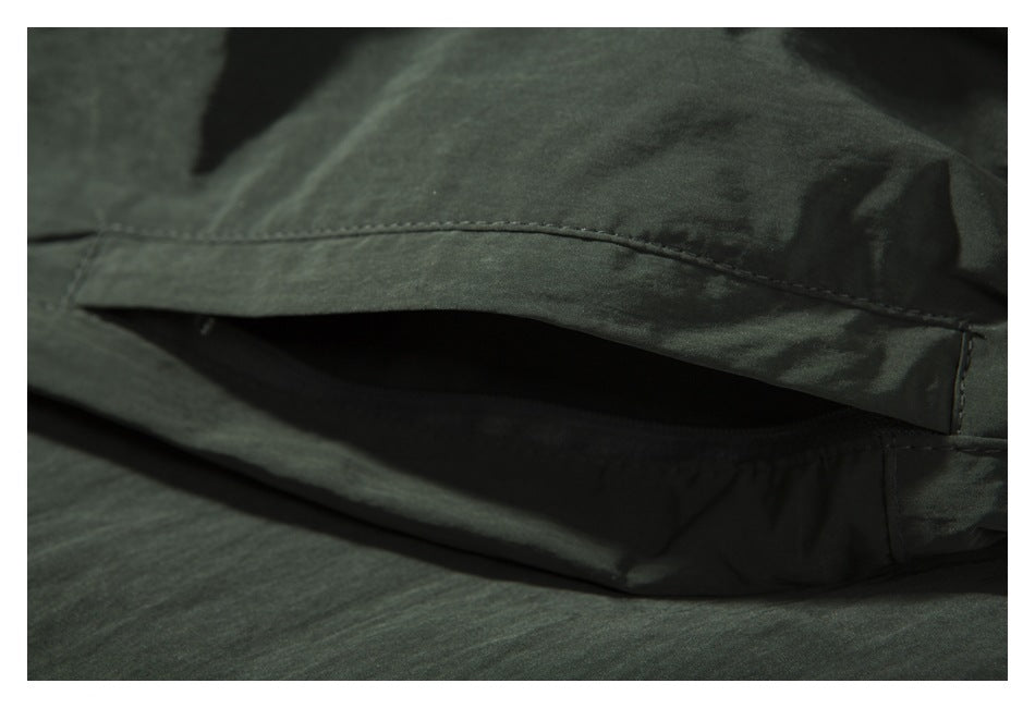 Close-up of a dark olive garment showing a stitched pocket opening.