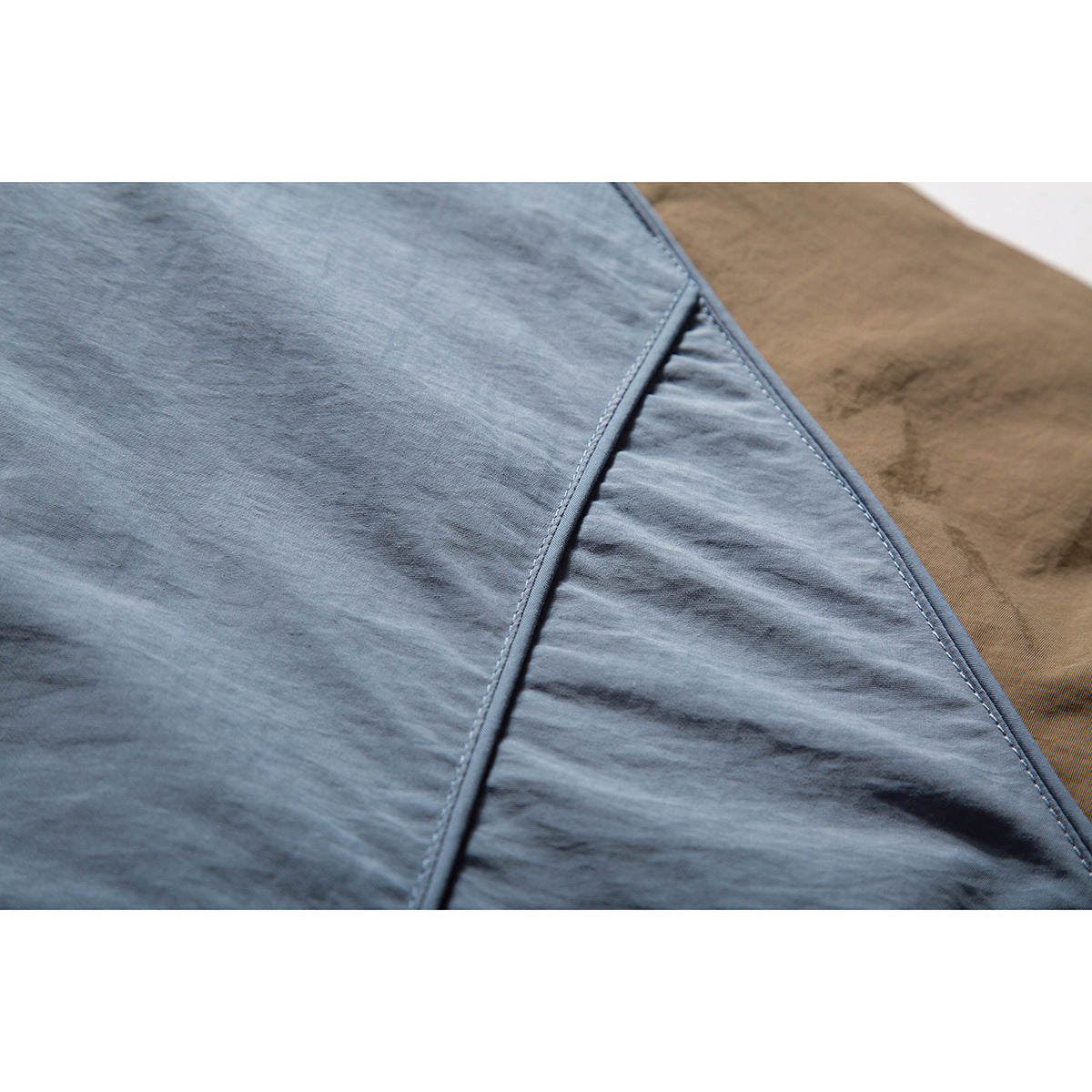 Close-up of slate-blue jacket panels with diagonal stitched seams and brown fabric at the edge.