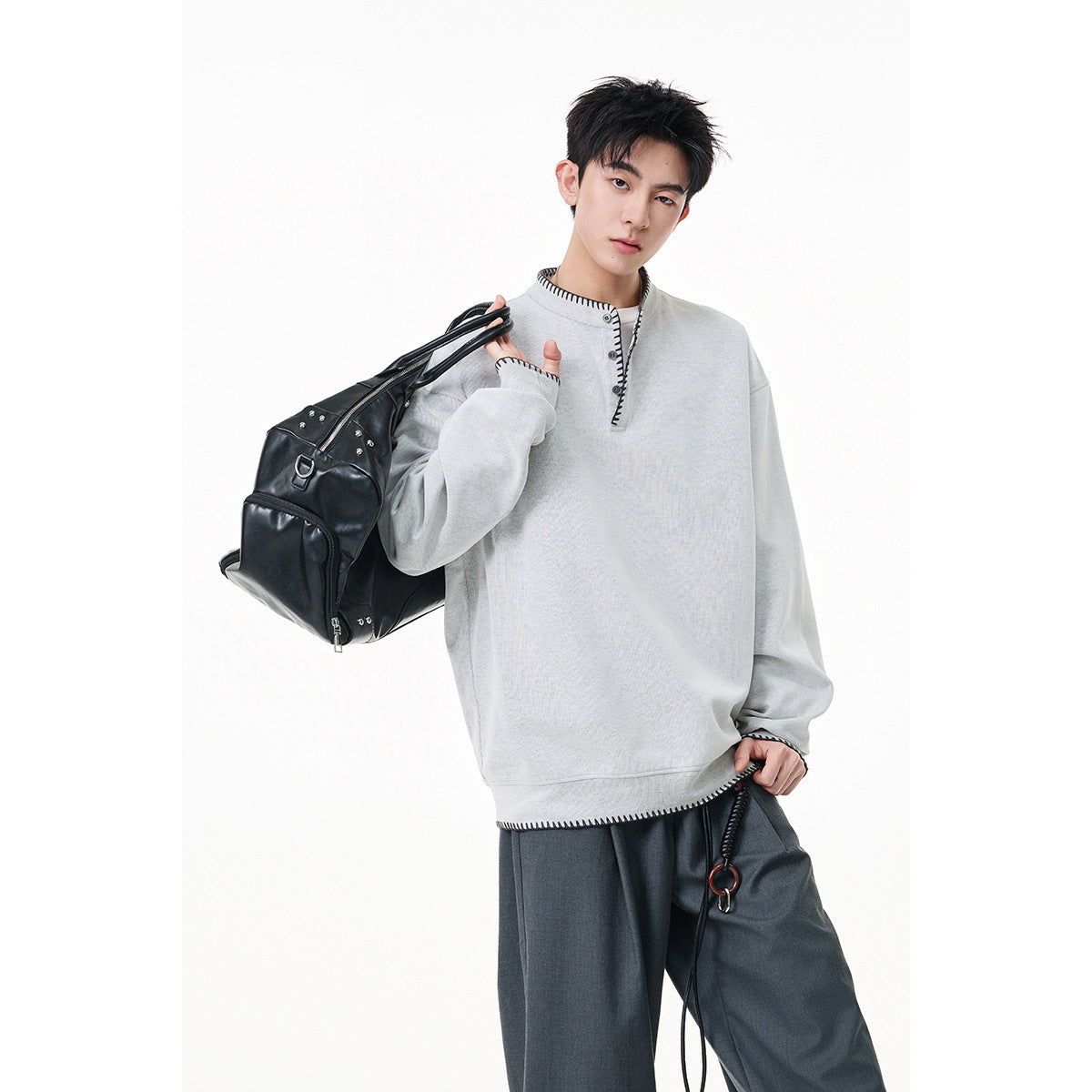 Man wearing an oversized light gray pullover with a short button placket and black contrast stitching.