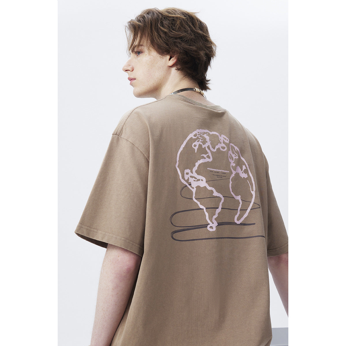 Close rear view of a model wearing a taupe oversized T-shirt with a large globe graphic.