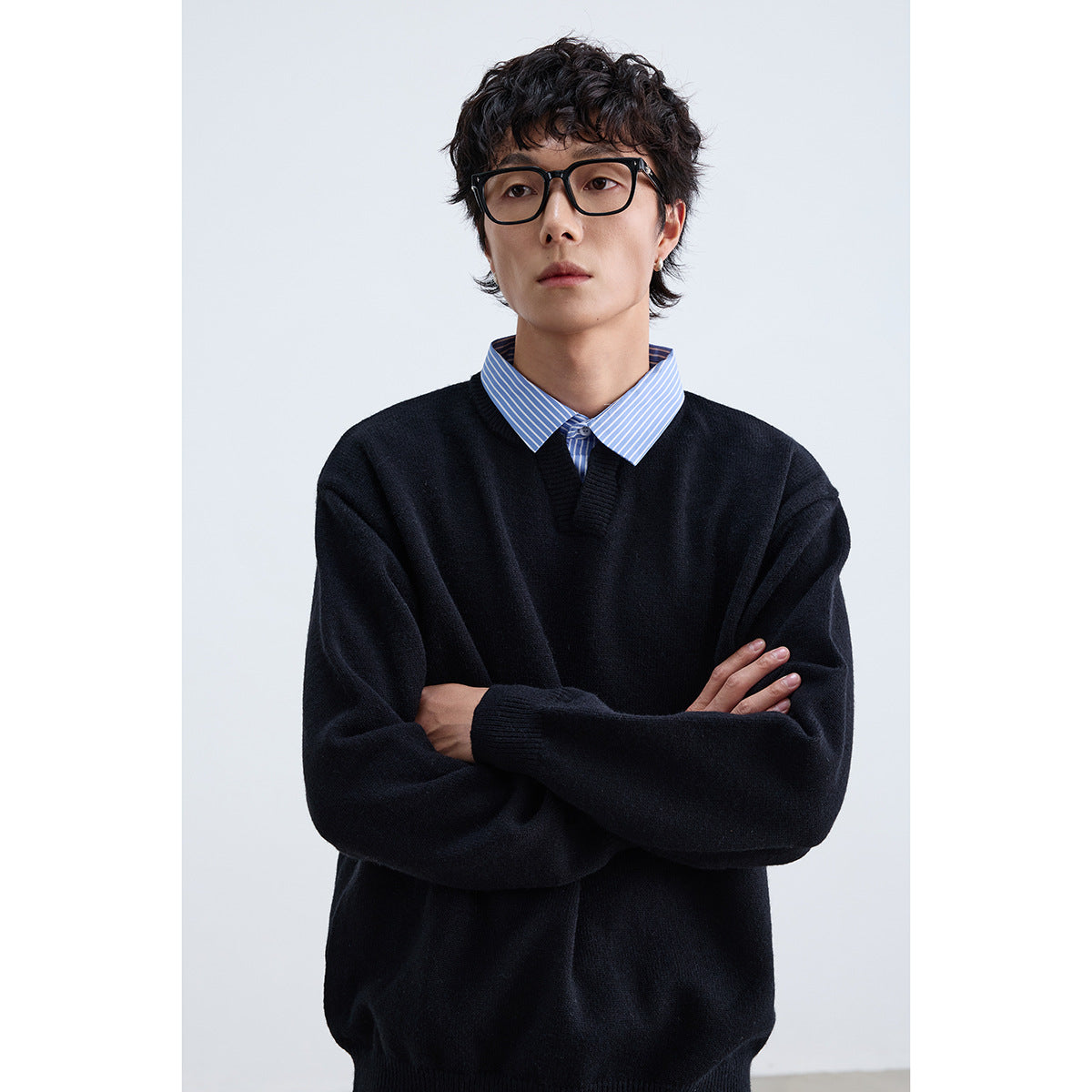 Model wearing a black V-neck sweater over a blue-and-white striped collared shirt.