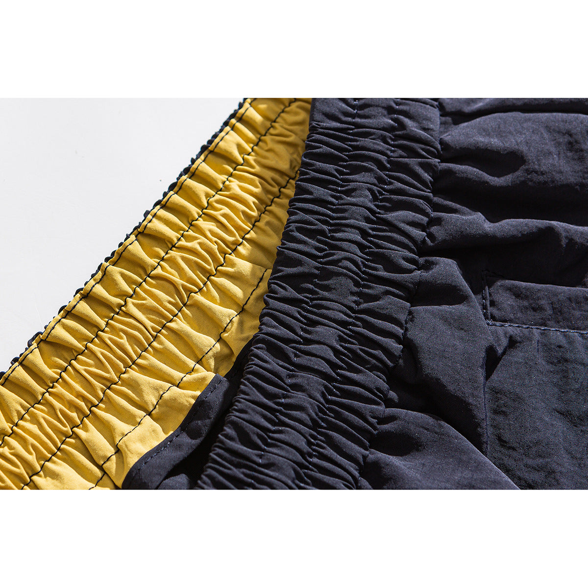 Close-up of the gathered waistband and contrasting yellow inner lining of dark shorts.