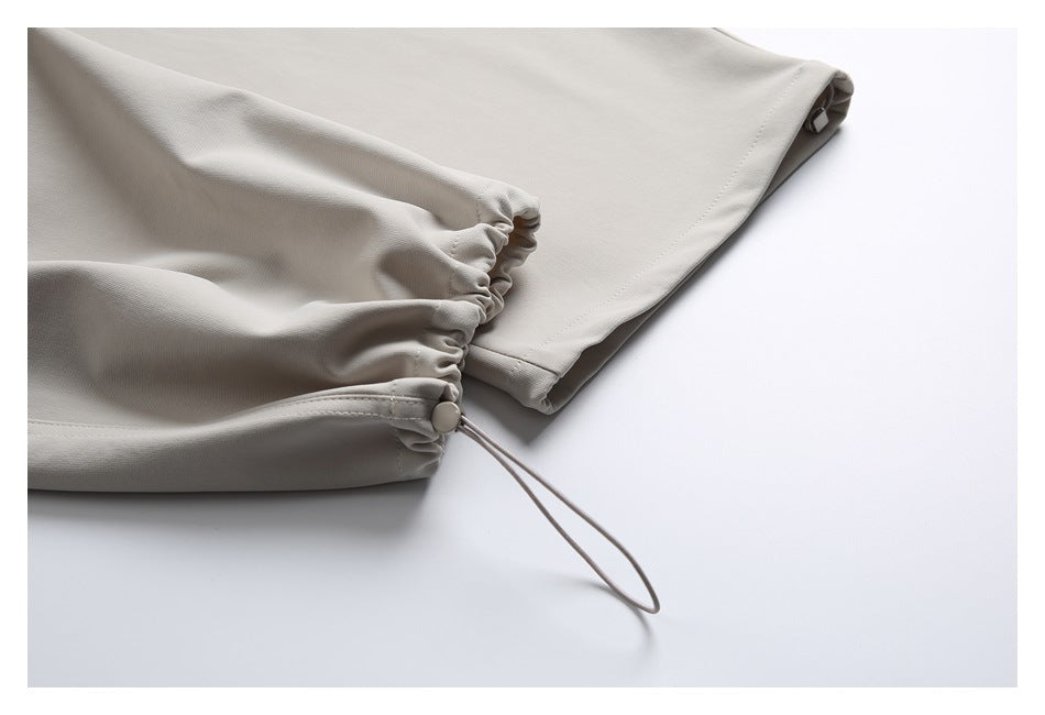 Close-up of a light beige trouser cuff with gathered elastic, a cord loop, and a round stopper.