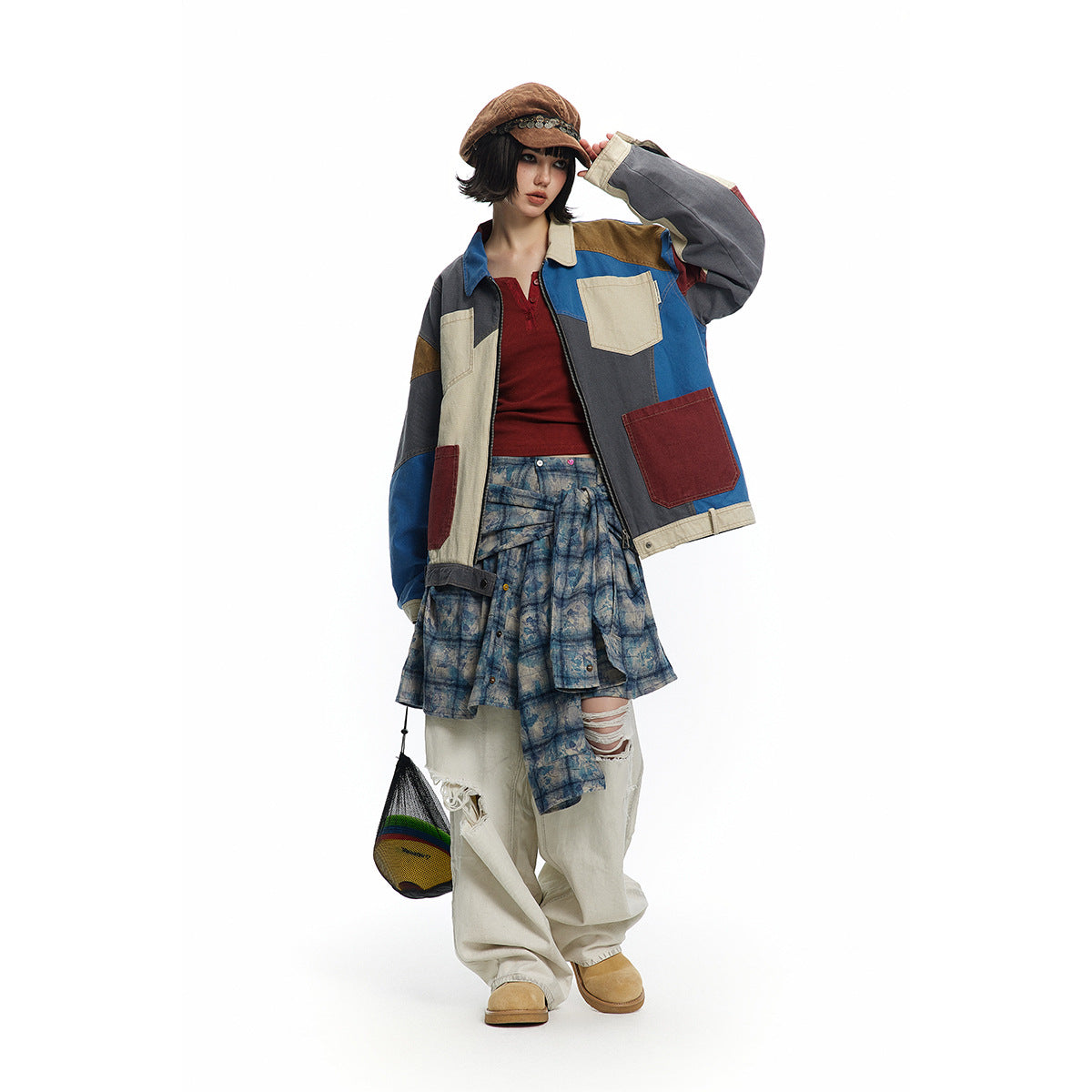 Model wearing a multicolor patchwork jacket with a blue patterned wrap skirt and loose cream trousers, shown from the front.