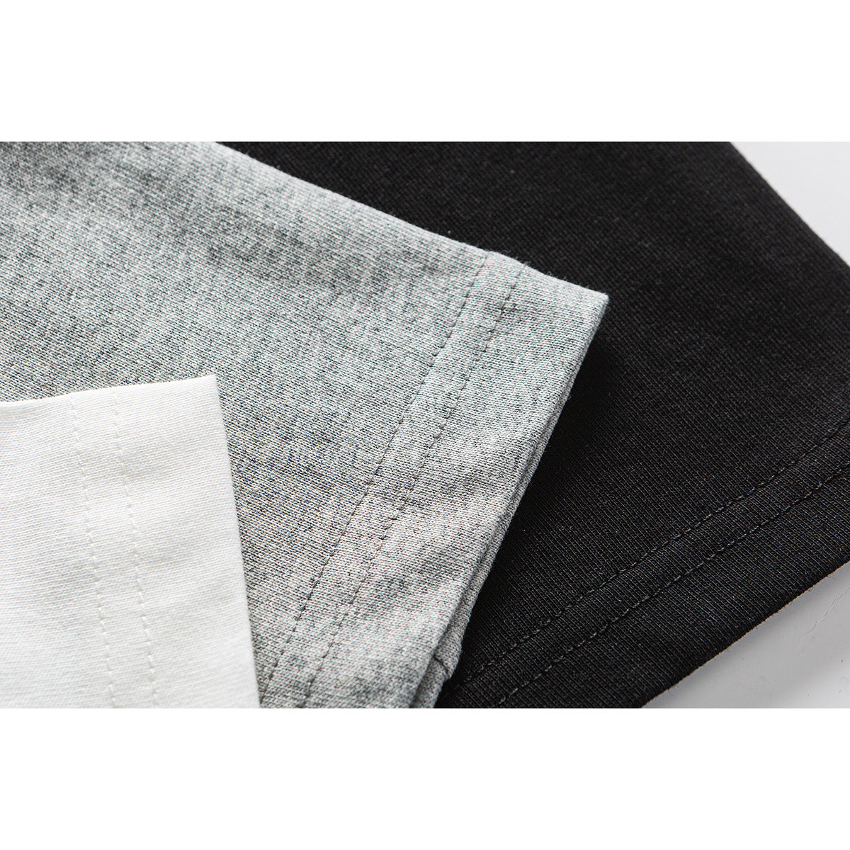 Close-up of stitched edges on white, heather-gray, and black T-shirt fabric.