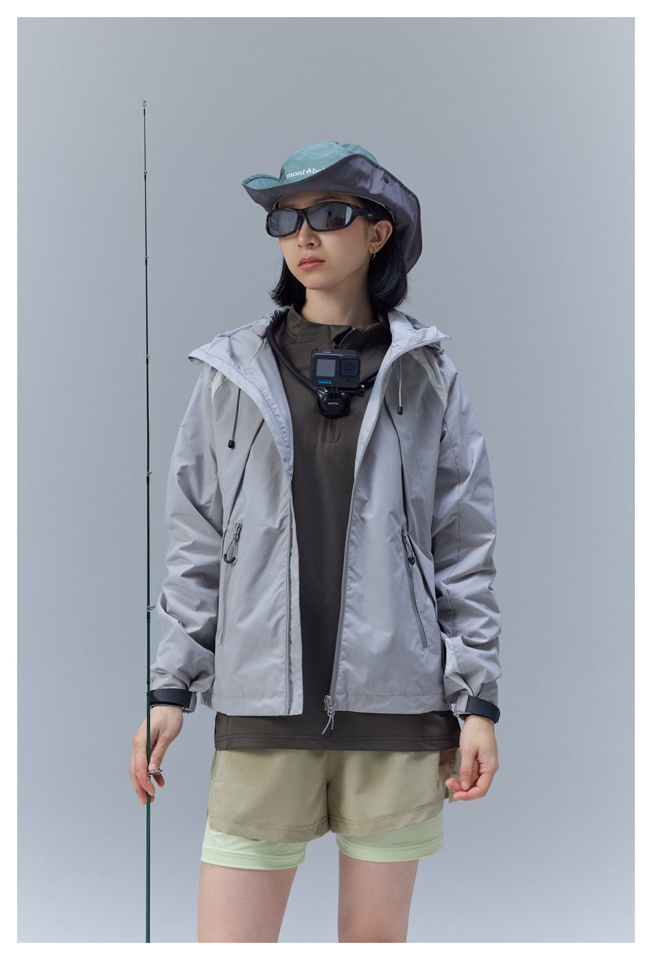 Woman wearing an open light gray hooded jacket with beige shorts, shown from the front.