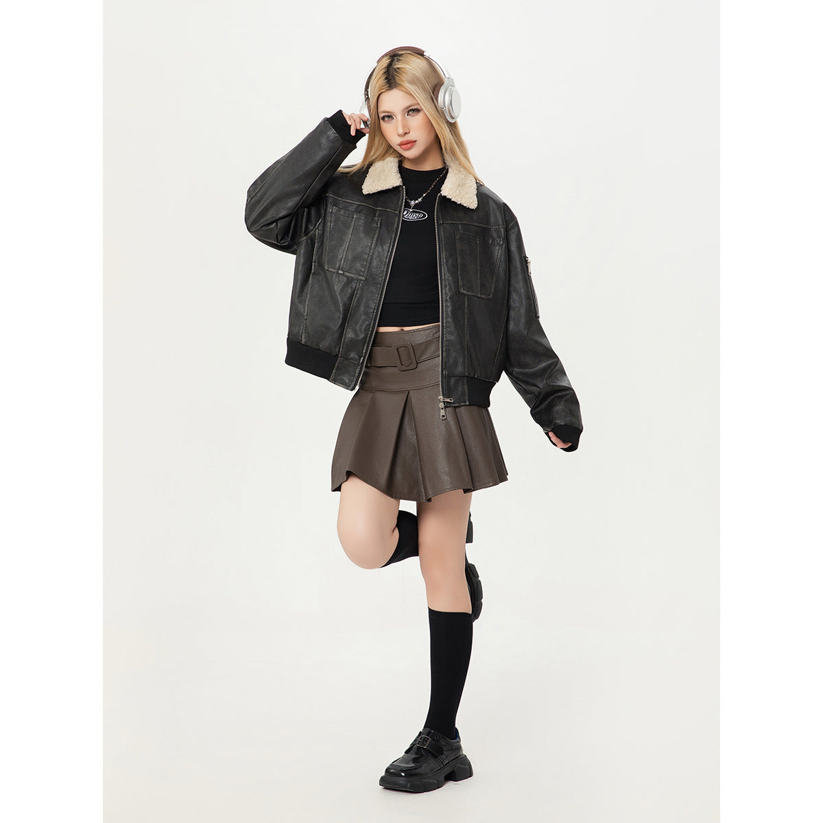 Model wearing a black jacket with a cream sherpa collar and a brown pleated mini skirt.