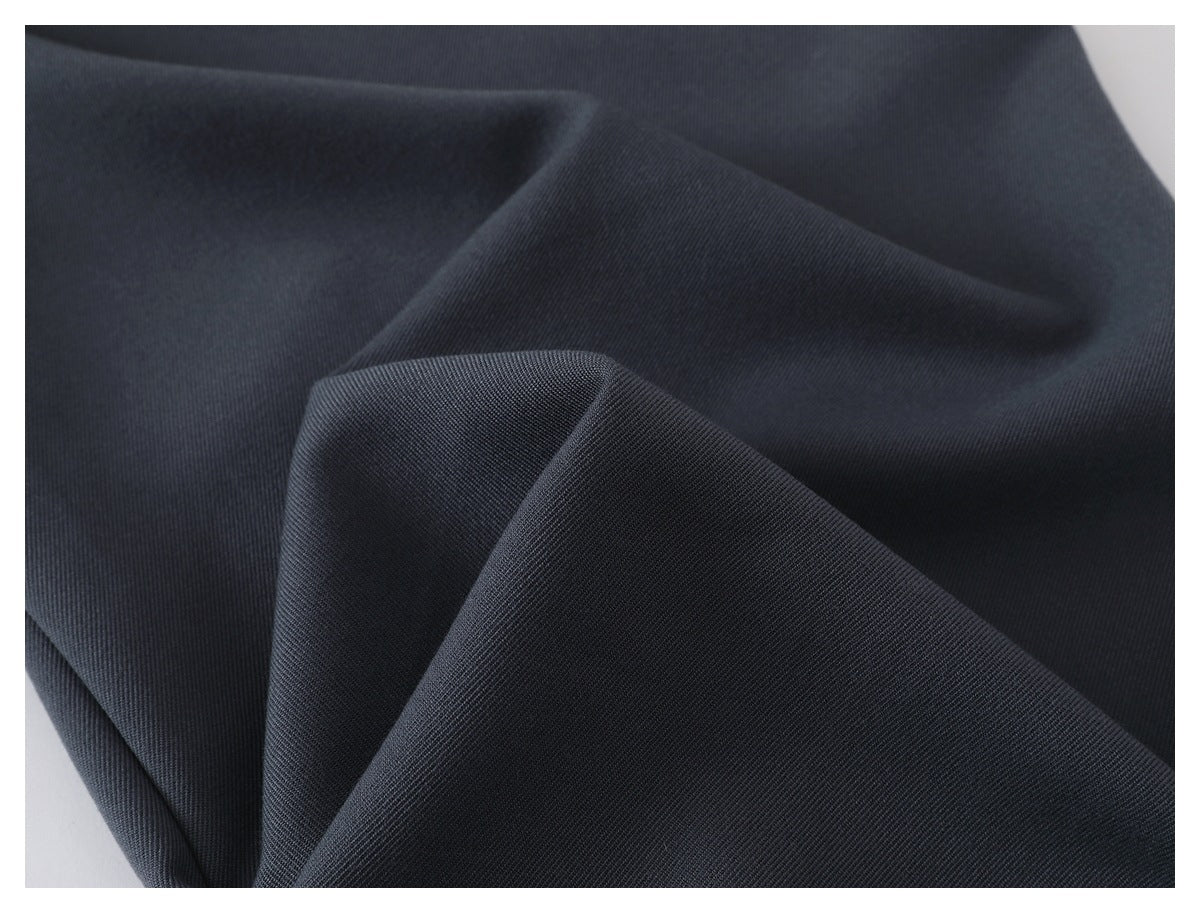 Close-up of charcoal trouser fabric folded to show its fine diagonal texture.