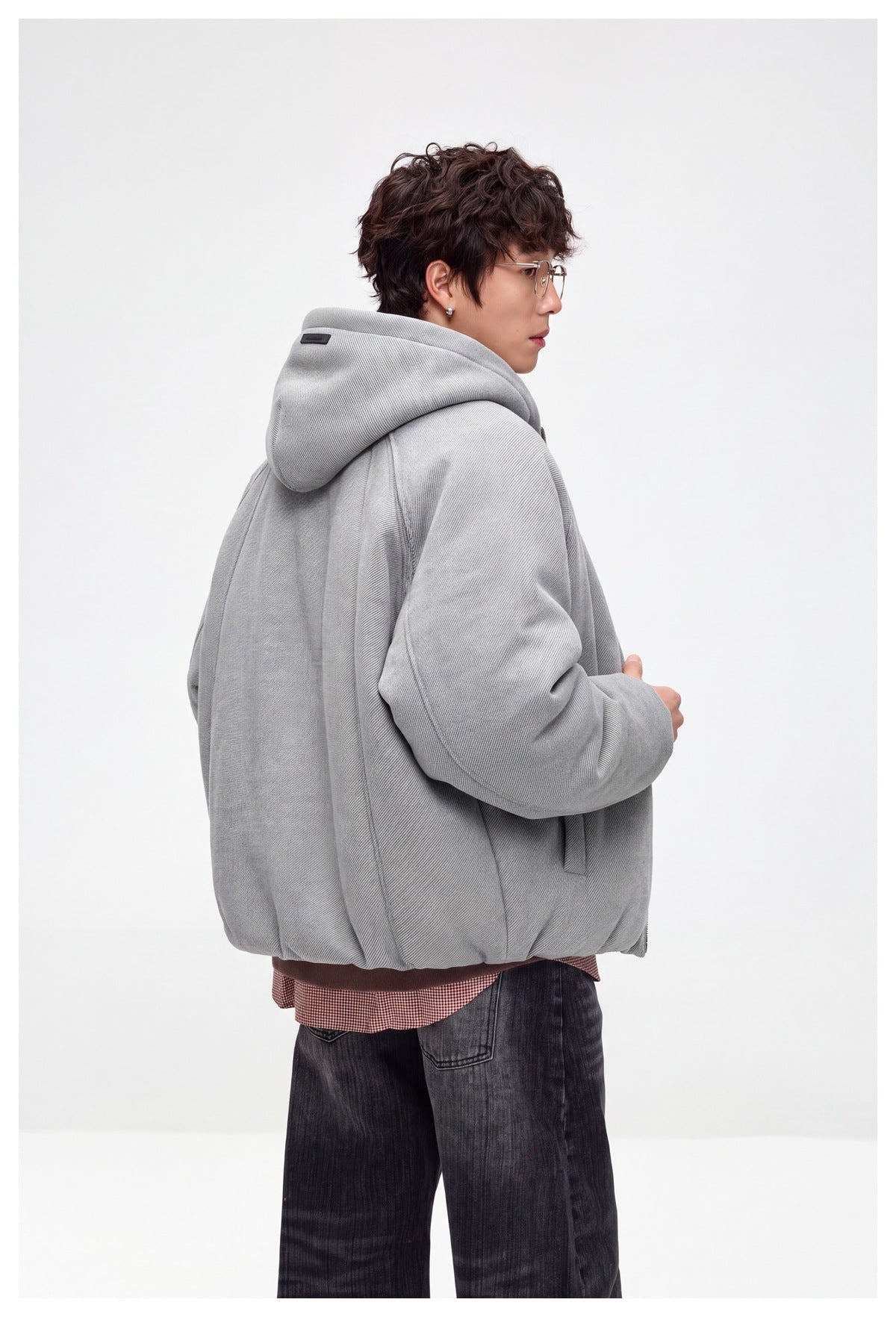 Side and back view of a model wearing a light gray hooded jacket with a small dark label on the hood.