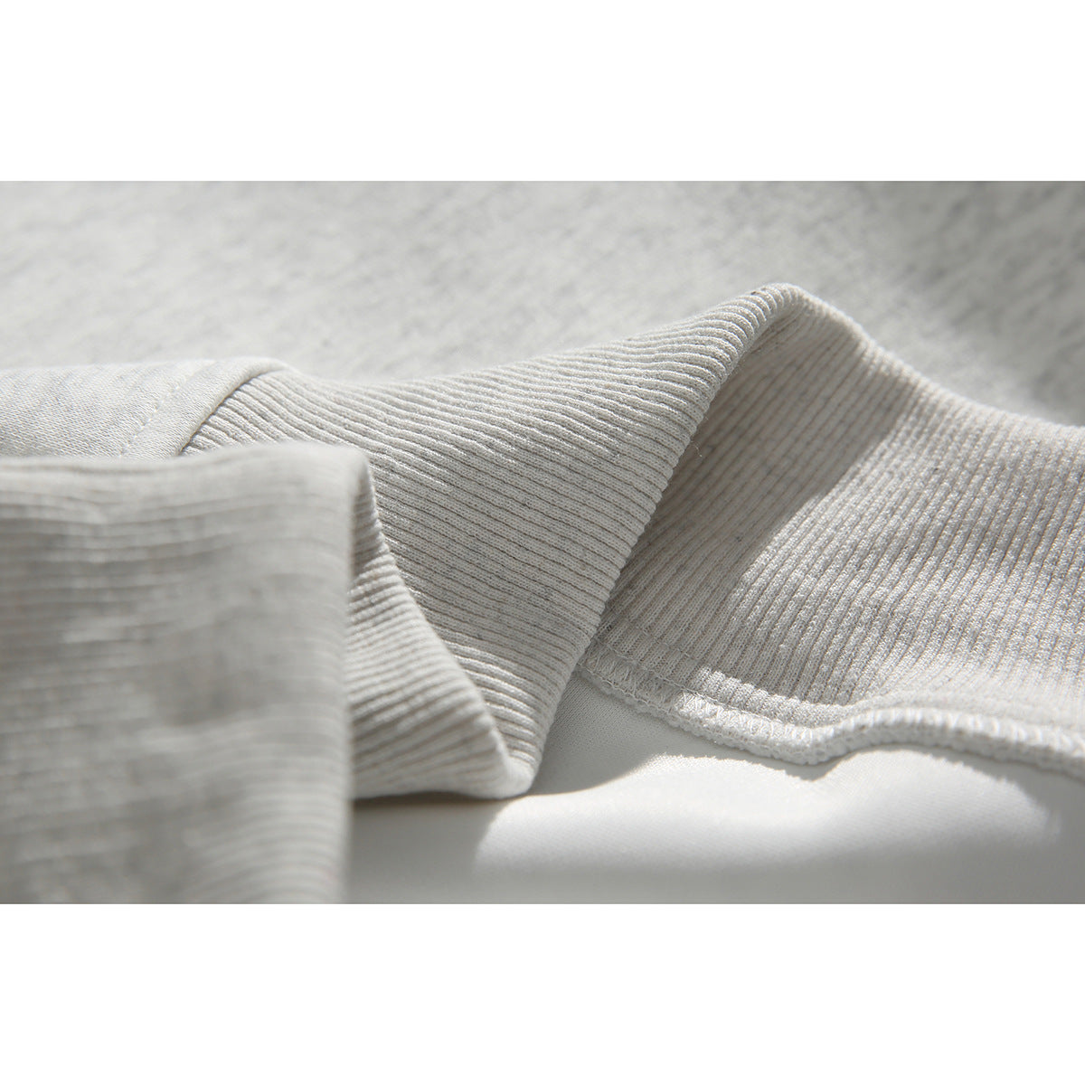 Close-up of the ribbed collar and cuff on a light gray sweatshirt.