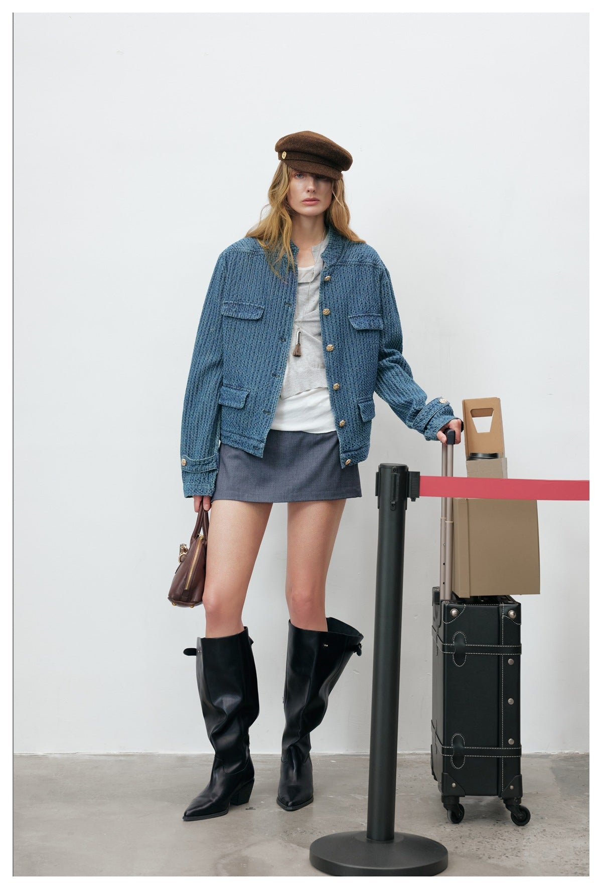 Woman facing forward in washed blue textured jacket with gold buttons, flap pockets, mini skirt and black boots
