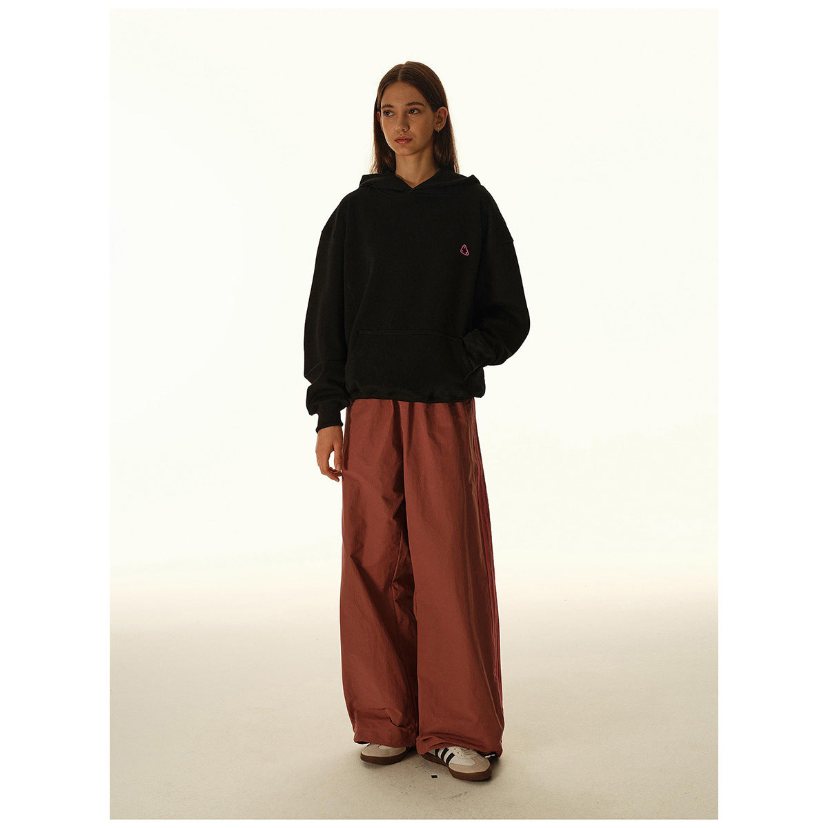 Full-length front view of a model wearing a black pullover hoodie and wide rust-red trousers.