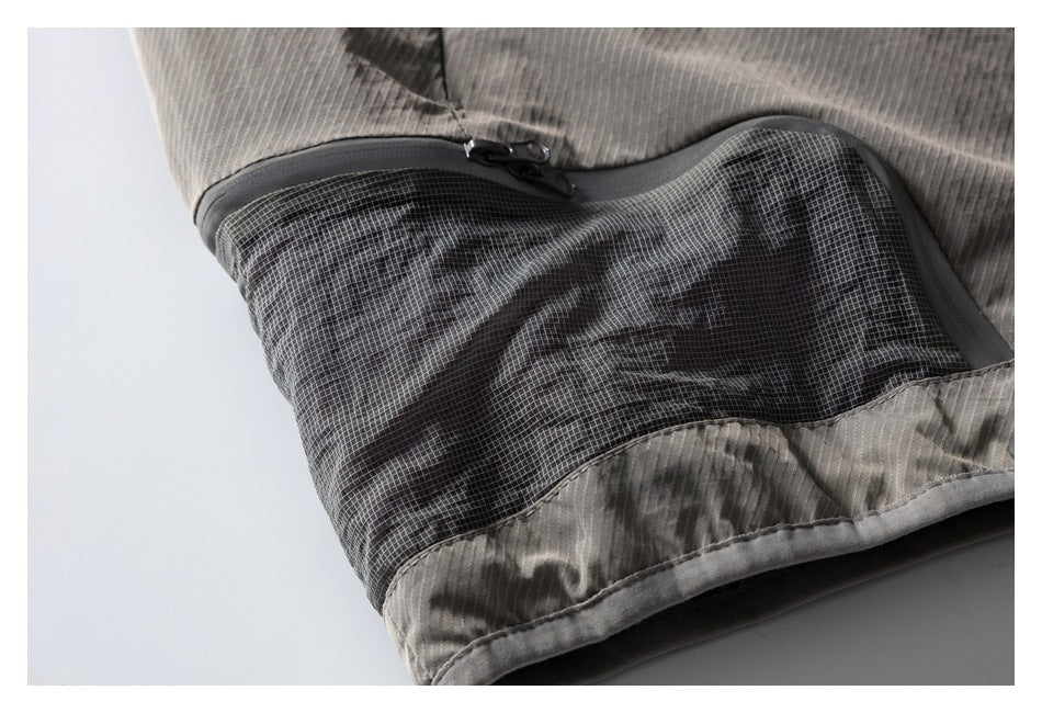 Close-up of a gray garment showing a black mesh pocket with a curved zip closure.