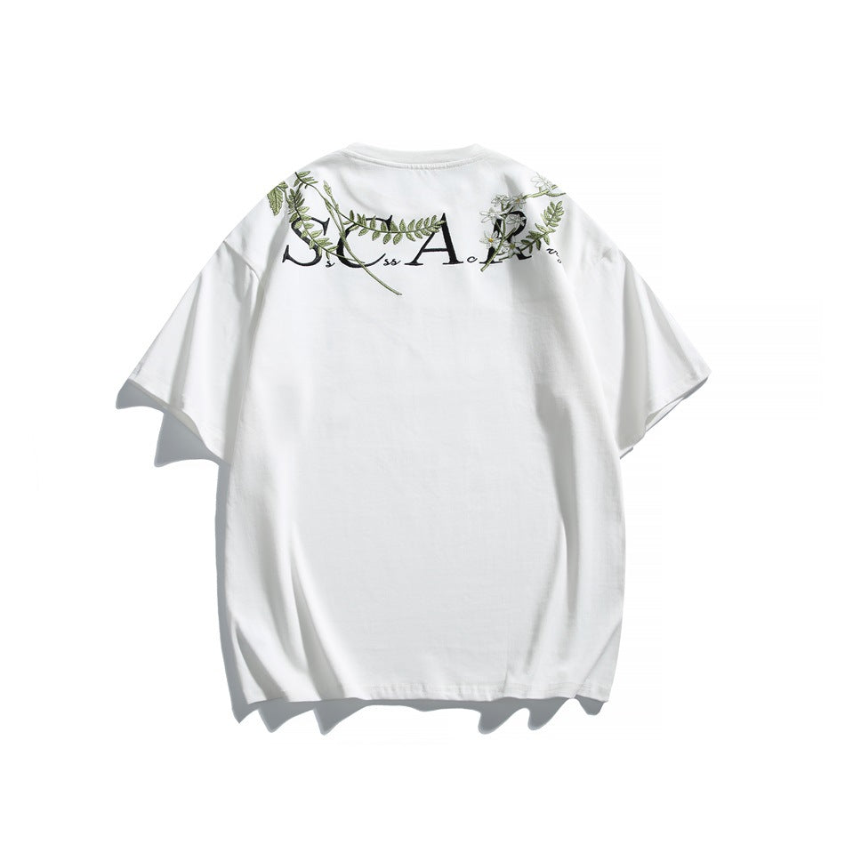 Back view of a white short-sleeve T-shirt with black lettering and green floral embroidery across the shoulders.